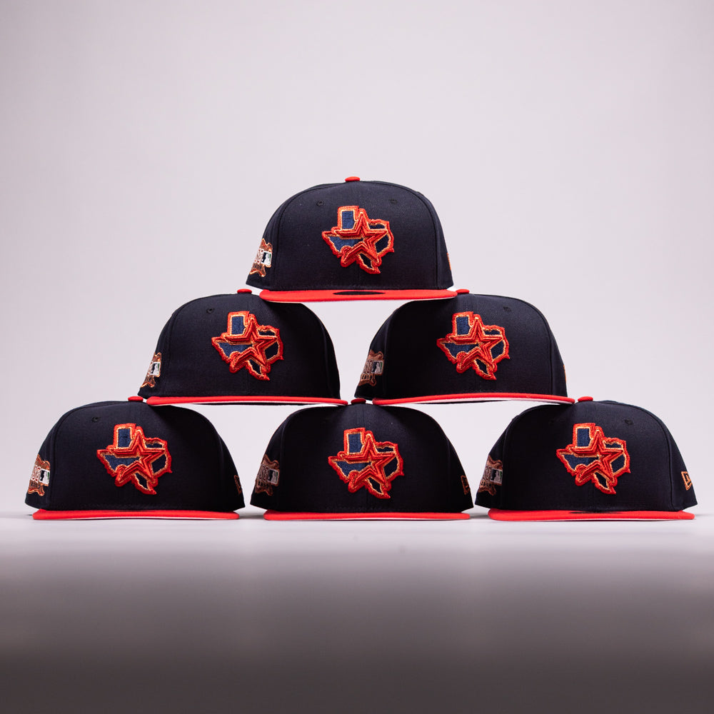 Six El Karma ASG Navy Red Houston Astros New Era Hat 5950 Fitted caps are stacked in a pyramid. Each navy hat has a red brim and showcases an embroidered red and orange Texas state outline with a blue accent, honoring the Houston Astros, along with side patches—all set against a plain background.