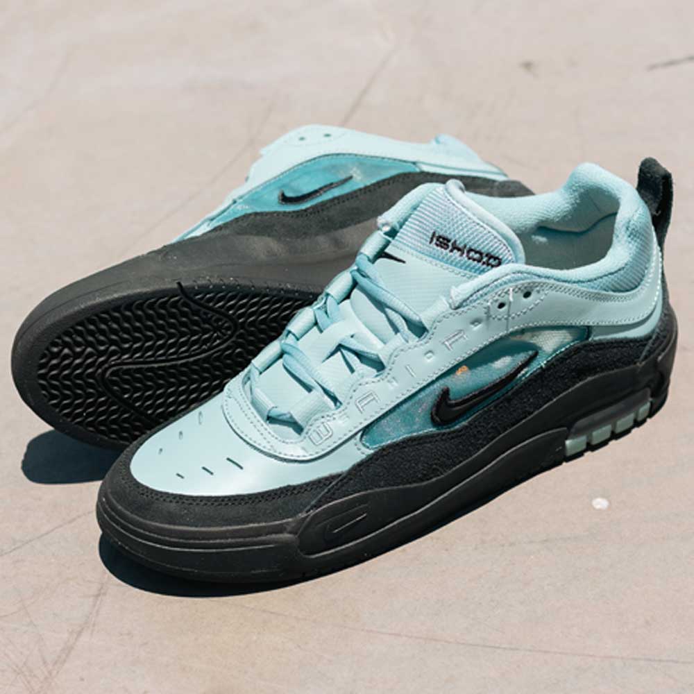 A pair of FB2393400 Denim Turq Black Denim Air MAX Ishod Nike SB skate shoes with black soles, made from suede and leather, showcase the Nike swoosh and Max Air cushioning, displayed on a light concrete surface.