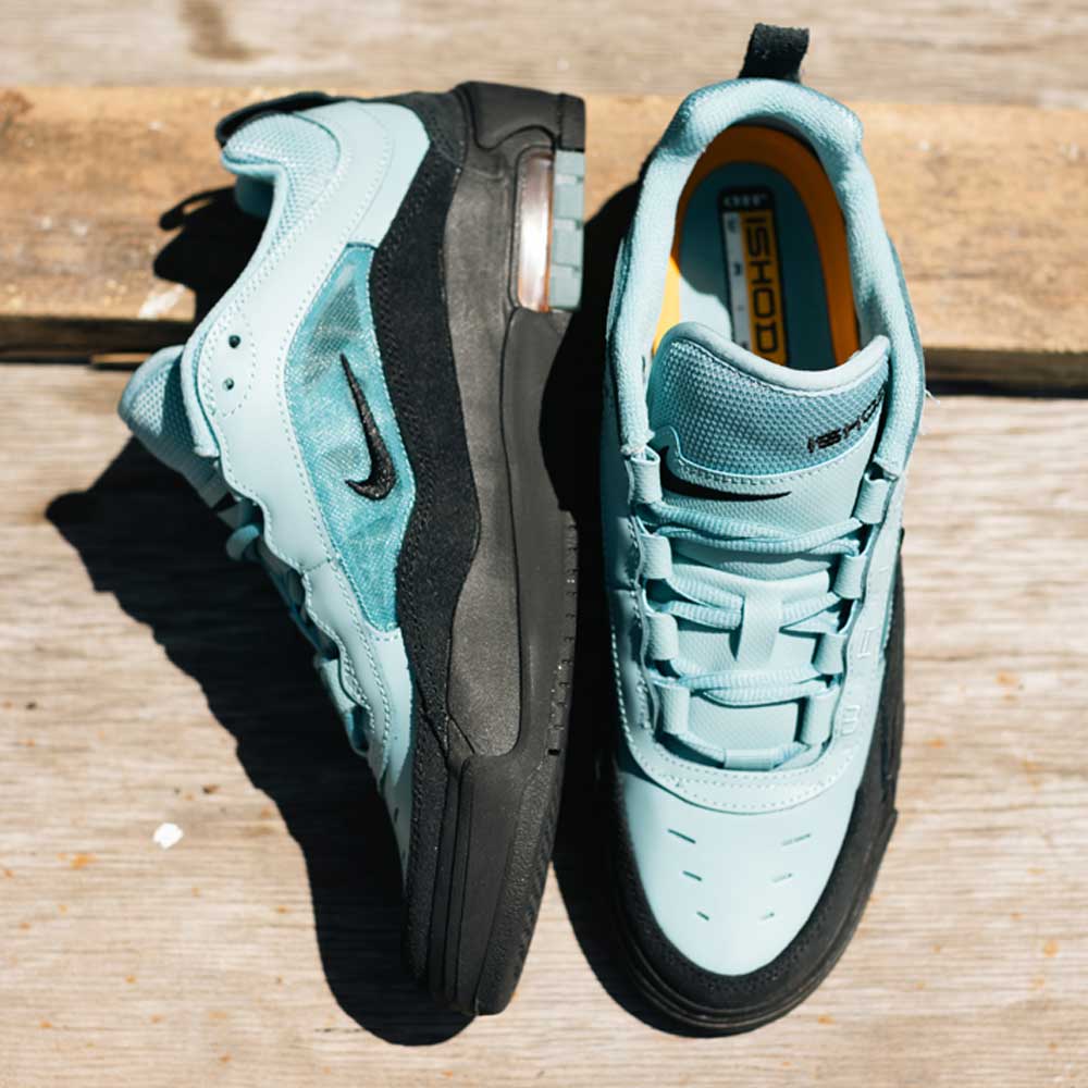 Two FB2393400 Denim Turq Black Denim Air MAX Ishod Nike SB suede leather skate shoes are shown on a wooden surface; one stands upright to display its side, while the other lies sideways, revealing the insole and Max Air cushioning.