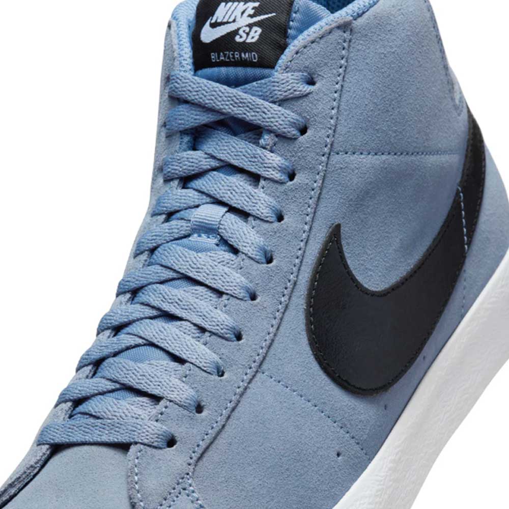 Close-up of the FD0731401 Ashen Slate Blazer Mid Nike SB suede shoes in light blue, featuring a black swoosh, white sole, black tongue label with white Nike SB branding, and Zoom Air cushioning for responsive support.
