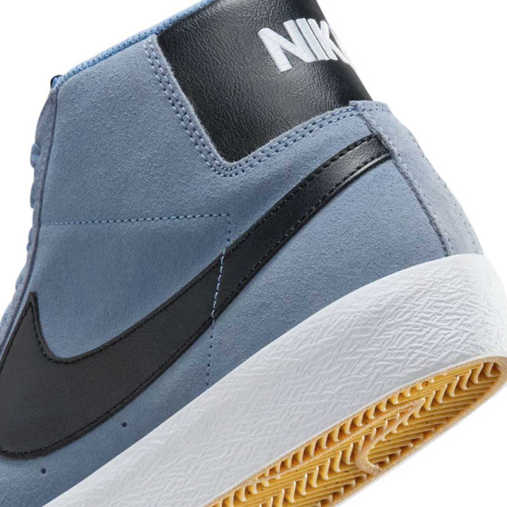 Close-up of the heel of the FD0731-401 Ashen Slate Blazer Mid Nike SB Suede Shoe in blue, featuring a black Swoosh, white NIKE text on a black heel patch, and a white rubber sole with textured gum outsole.