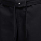 Close-up of the waistband on the FV7349010 Double Knee Pant Black Nike SB Skateboarding, featuring black cotton twill fabric, a drawstring tie, and a small silver button at the top center.