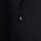 Close-up of black cotton twill fabric from the FV7349010 Double Knee Pant Black Nike SB Skateboarding, showing a small black tag with the white Nike SB logo near a seam, likely on a pocket.