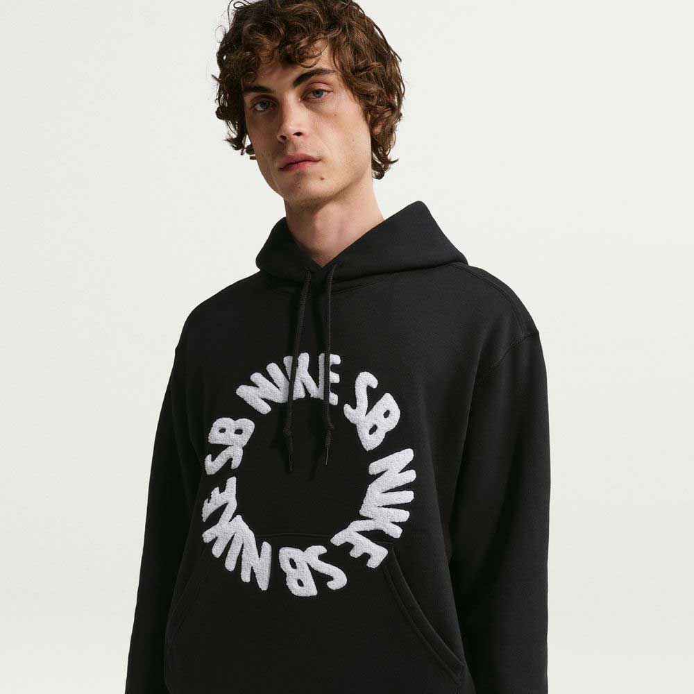 A youth with curly brown hair wears the Nike SB Fleece Pullover Black White IF0655-010 hoodie, featuring a white circular logo on the front and a relaxed fit, standing against a plain white background.