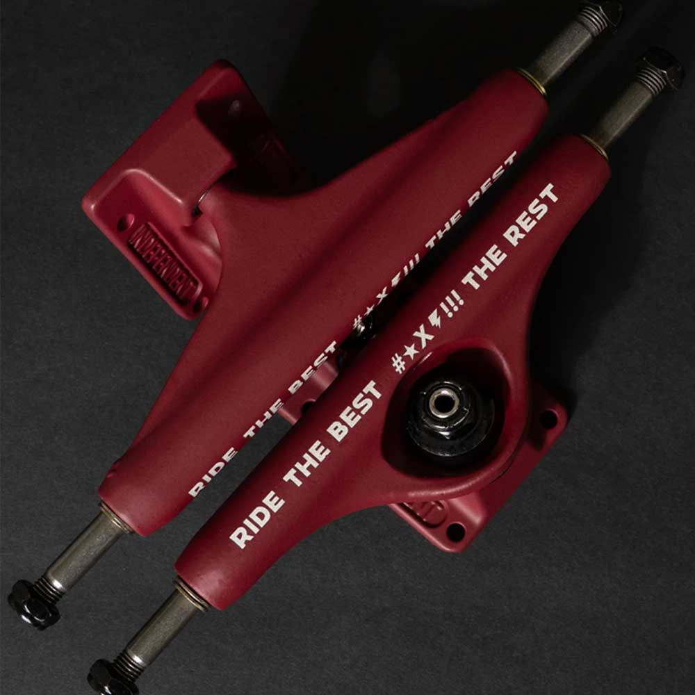 Two Forged Hollow RTB FTR Burgundy Standard INDY 144 Stage 11 Trucks are crossed on a dark surface. One lightweight, durable skateboard truck displays "RIDE THE BEST #!XX!!! THE REST" in white, with metal axles and black details. Set of two.
