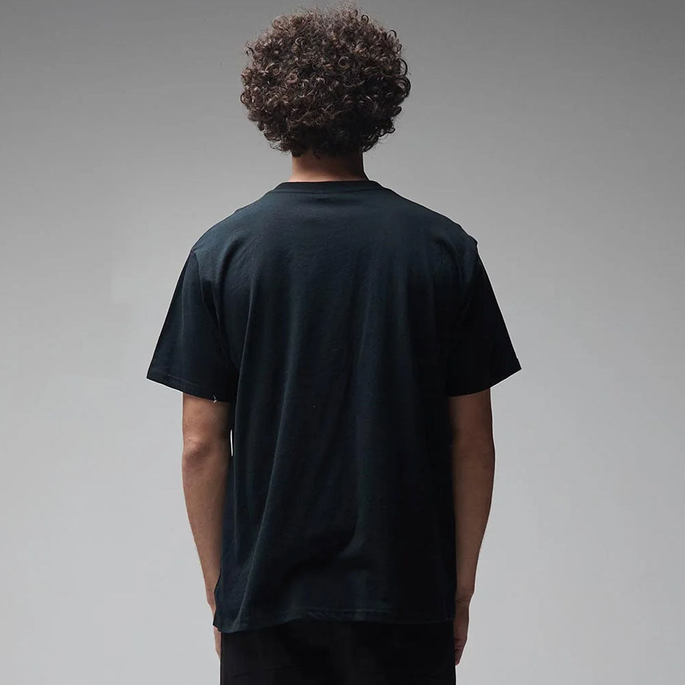 A person with curly hair is standing with their back to the camera, wearing the Mind Glass Former Tee Black—a plain black 200GSM cotton T-shirt—against a neutral gray background.
