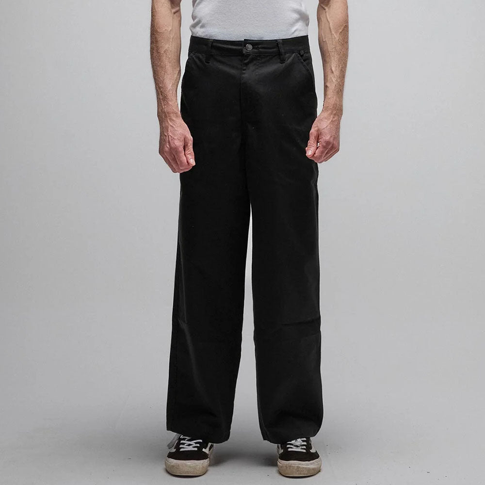 A person wearing a white t-shirt, black Reynolds Work Pant Black Former, and black sneakers with white soles is standing against a plain gray background. Their face is not visible.
