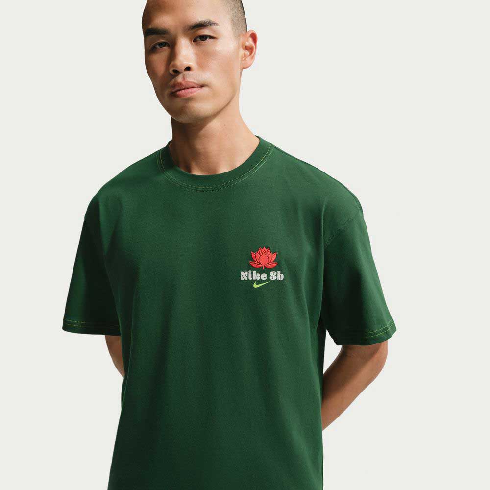 A person wears the Nike SB Gorge Green Som Tum Dunk Tee (IH1478341), a dark green midweight cotton skateboarding t-shirt with a red lotus flower and Nike SB text on the left chest, standing against a plain white background.