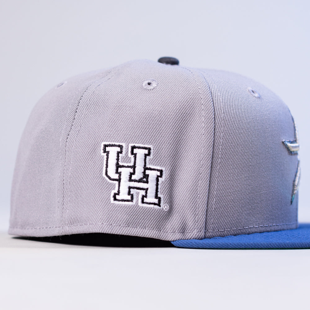 The Peoples Champ Gray Blue Houston Cougars New Era Hat 5950 Fitted features a light gray design with a blue brim and an embroidered white UH logo outlined in black on the side, showcasing classic Houston Cougars style.