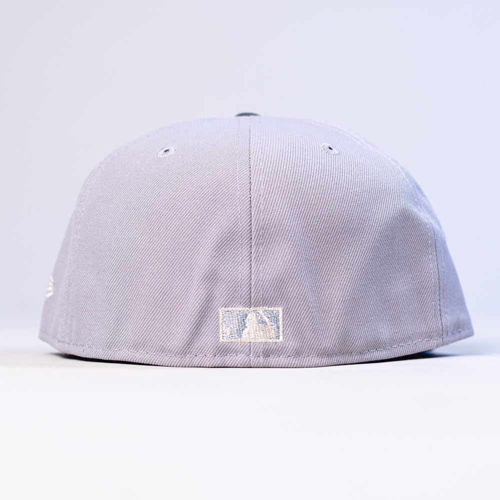 A light gray and blue Peoples Champ Houston Cougars New Era Hat 5950 Fitted is displayed from the back, highlighting a small white rectangular logo at the center bottom and ventilation eyelets on top. This fitted cap provides both comfort and classic Houston Cougars style.