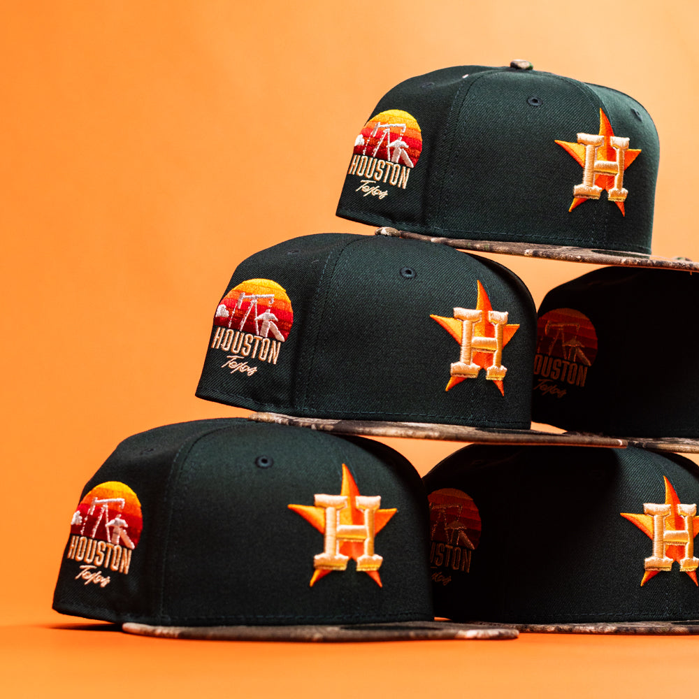 Several Greenhand RTC Oil Houston Astros New Era Hat 5950 Fitted caps, featuring unique patch designs, are stacked in a pyramid against an orange background.