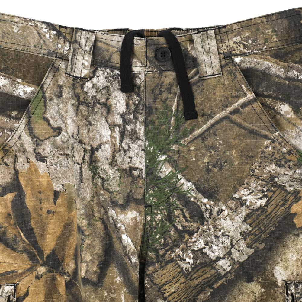 Close-up of the Groundwork 2 Cargo Pants Realtree APX Bottom Mens Independent, a camouflage-patterned ripstop cargo pant featuring belt loops, a black drawstring, button closure, and front pockets; designed in the Realtree APX colorway of brown, green, and tan for durable style inspired by Independent Trucks apparel.
