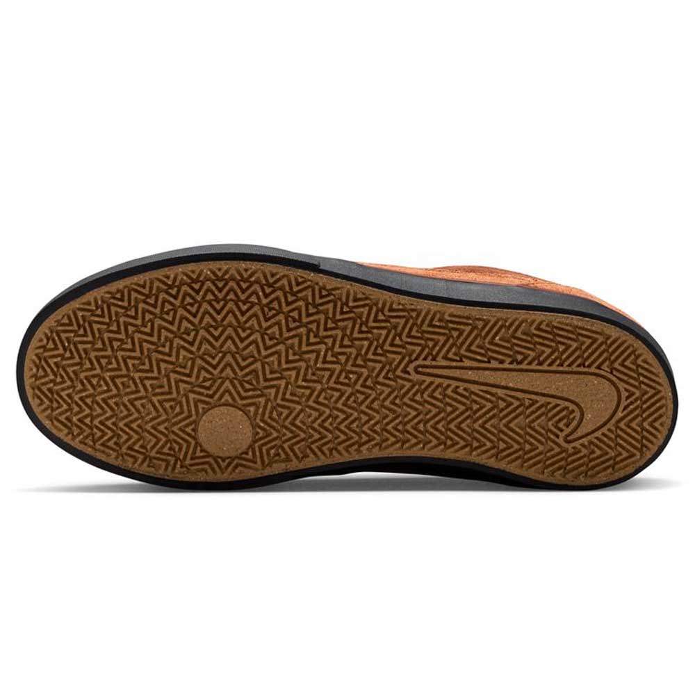 The image shows the sole of a Nike SB Malor GS youth skate shoe (HF1205200 Cinnamon Light Bone) with a brown, textured rubber bottom featuring a herringbone pattern, circular design by the ball of the foot, and an embossed Nike Swoosh. The upper is orange.