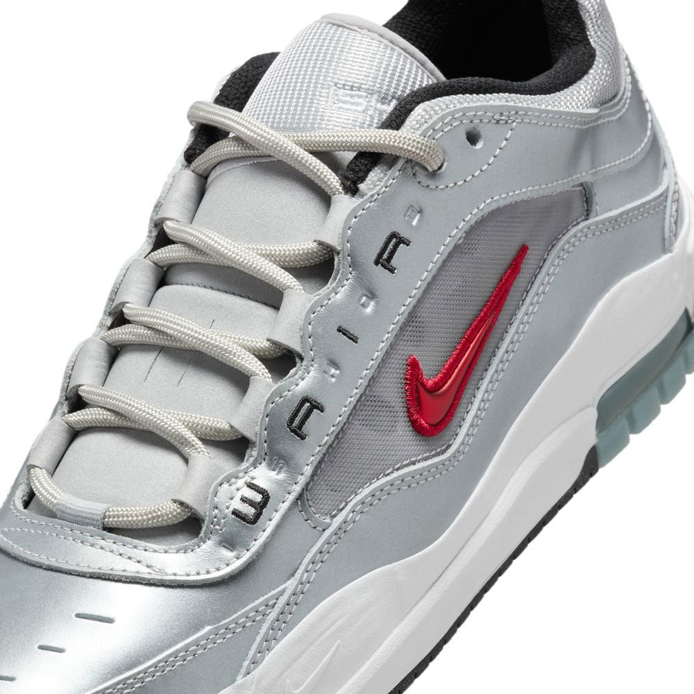 A close-up of the HF3062001 Silver Bullet Air Max Ishod Wair leather and suede shoe, featuring a metallic silver finish, red Nike Swoosh, white sole, visible Max Air heel unit, and unique lacing inspired by classic skate shoes.