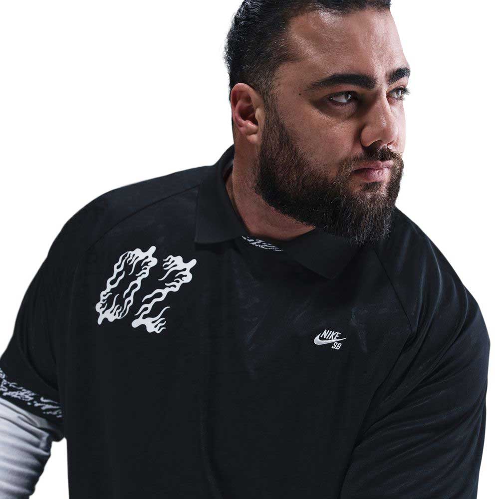 A man with dark hair and a beard wears the HJ 2965010 Black Nike SB Dri-FIT Jacquard Skate Jersey Skateboarding, featuring a white chest graphic, as he looks to his right against a white background.