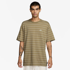 Someone wearing the HJ0812297 U NK SB TEE M90, a tan and white striped Nike SB Skateboarding tee with a small logo on the chest, stands against a plain white background.