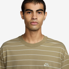 A person with short dark hair wears the HJ0812297 U NK SB TEE M90 Tan White STRIPE Nike SB Skateboarding tee, standing against a plain white background and looking directly at the camera.