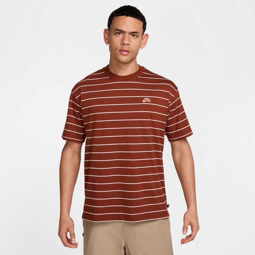 A young man stands facing forward, wearing the HJ0812619 U NK SB TEE M90 Maroon Red STRIPE by Nike SB Skateboarding and tan shorts, against a plain light background.