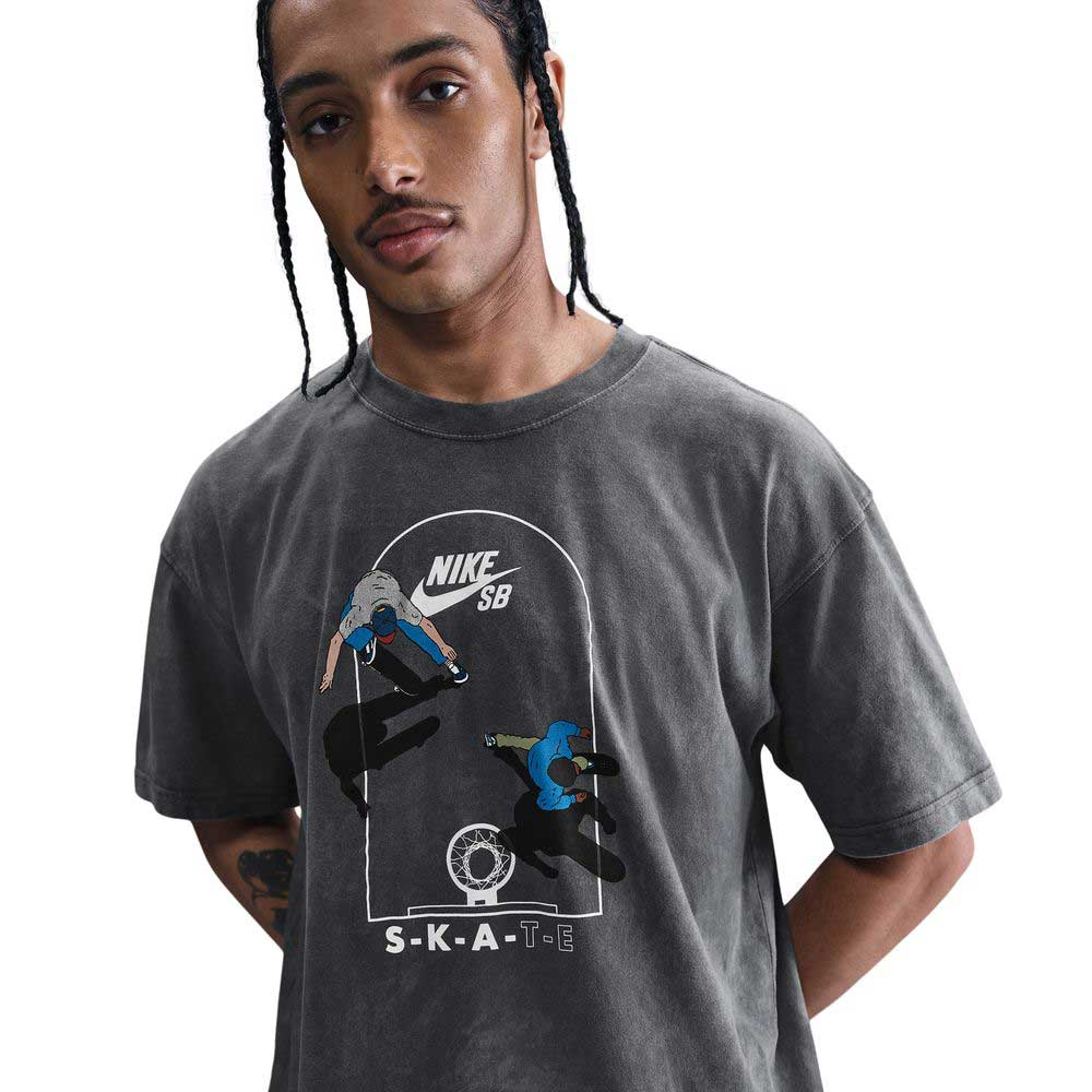 A person with braided hair wears the HJ0816060 Max 90 Skate T-Shirt— a gray Nike SB tee with a roomy fit, midweight cotton, and colorful skateboarding screenprinted graphics featuring "SKATE" on the front.