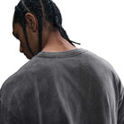 A person with braided hair is shown from behind, wearing the HJ0816060 Max 90 Skate T-Shirt SB Tee in faded gray. The loose, midweight cotton Nike SB shirt stands out against a white background, highlighting the back and shoulders.