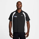 A man stands facing forward, wearing a HJ2956010 Black White Dri-Fit Woven Short-Sleeve Bowler Shirt by Nike SB Skateboarding, featuring embroidery and a chest pocket.