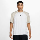A man stands facing forward in the HJ2956010 Light Gray White Dri-Fit Knit Skate Jersey by Nike SB Skateboarding, featuring embroidered details, paired with black pants against a plain white background.