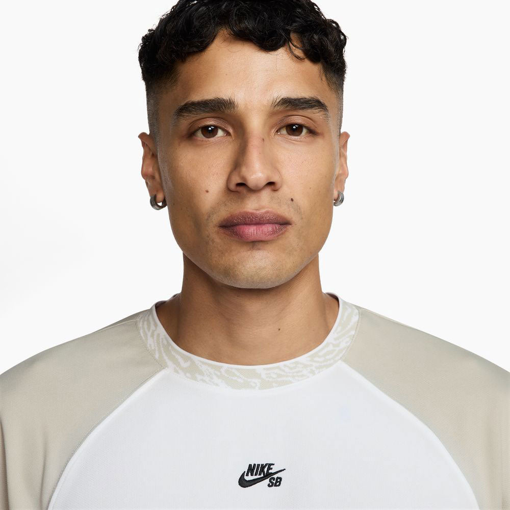 A young man with short, curly dark hair and hoop earrings looks at the camera, wearing the HJ2956010 Light Gray White Dri-Fit Knit Skate Jersey by Nike SB Skateboarding, featuring embroidered details. The background is plain white.
