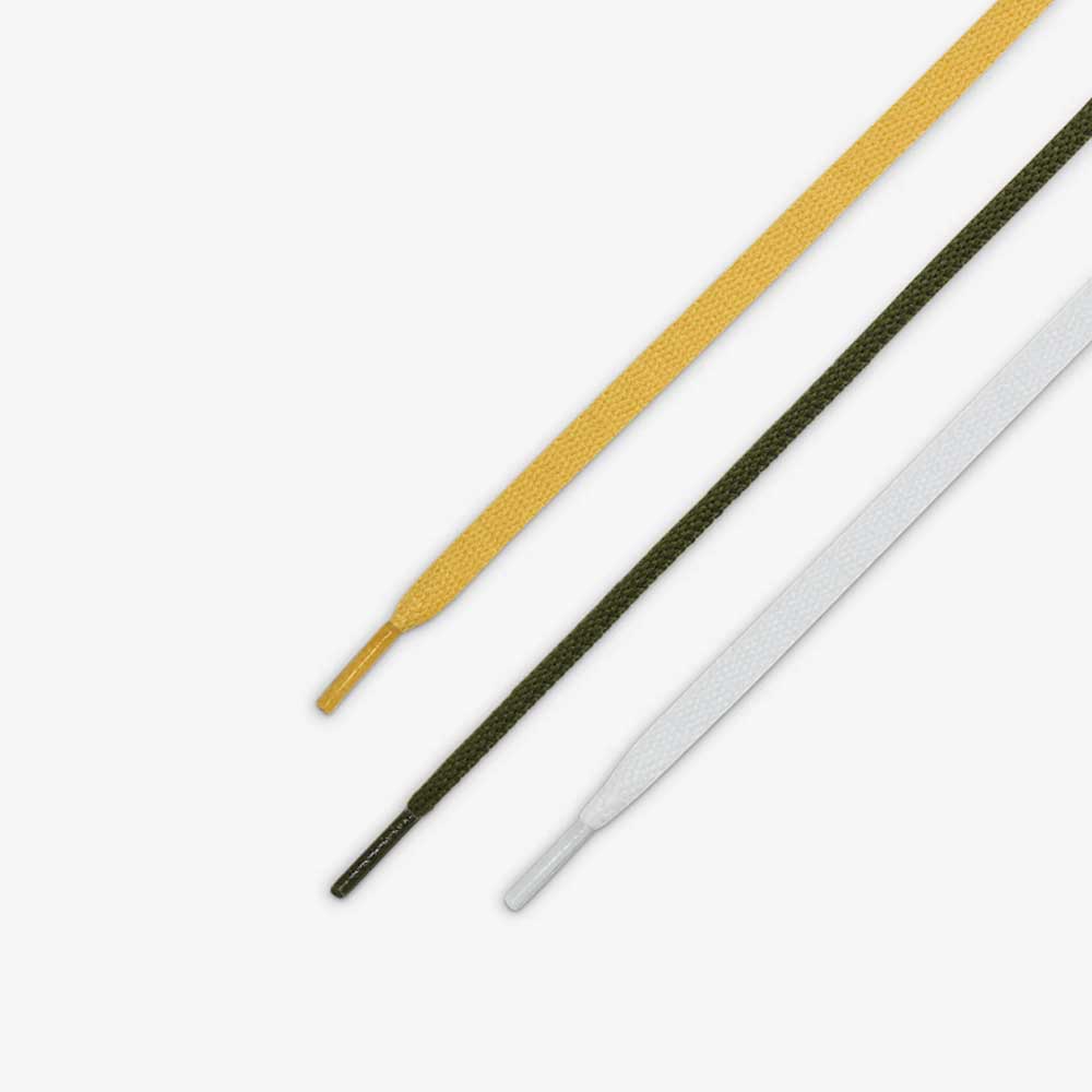 Three shoelaces—yellow, dark green, and white—are laid parallel on a white background, echoing the colorway of HM5838300 Anti Hero Rough Green Amarillo Blazer Mid Nike SB suede skateboard shoes. Each lace ends with a plastic aglet.