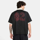 A man with curly hair, seen from the back, wears the Nike SB HV4457010 Polo Skate T-Shirt in black with white collar and cuffs, featuring a bold red "02" graphic on the back. Made of 100% cotton and machine washable for easy care.