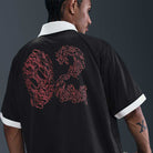 A person with braided hair wears the Nike SB HV4457010 Polo Skate T-Shirt in black, red, and white, featuring a bold flame-red 92 on the back. Made of 100% cotton with standout white collar and cuffs. Easy care—machine washable.