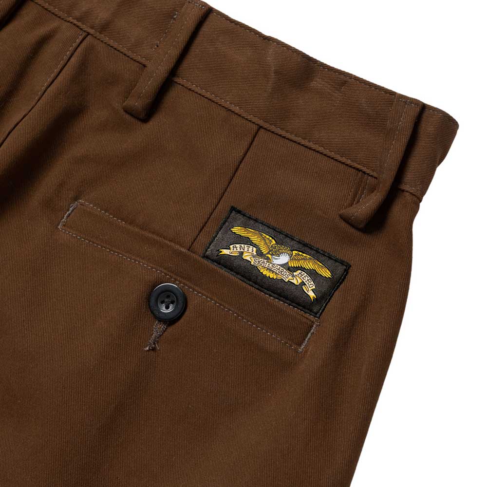 The Hecho Por Skate Pant by Anti Hero Skateboards in brown features a back pocket with a black button and a rectangular patch above it showing an eagle with arrows—ideal for Skateshop Day or celebrating exclusive skateboard drops.