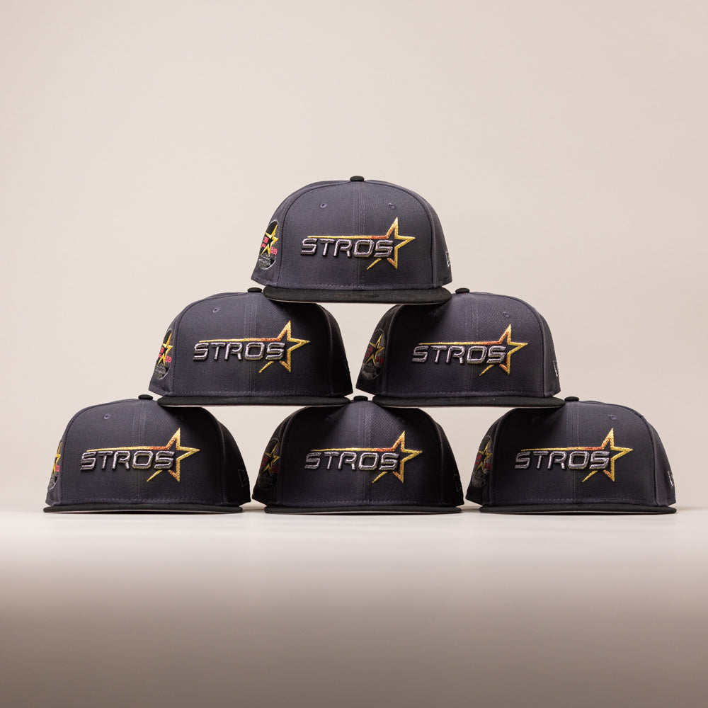 Six dark grey Black Delta City Connect Houston Astros New Era Hat 5950 Fitted caps stacked in a pyramid, each featuring a yellow and red star logo with the word STROS embroidered on the front.
