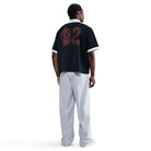 A person stands facing away, wearing a black short-sleeve shirt with “02” in red on the back, IB2992085 Skate Trousers Pant Loose Fit Straight Leg Nike SB Light Blue, and white sneakers against a plain white background.