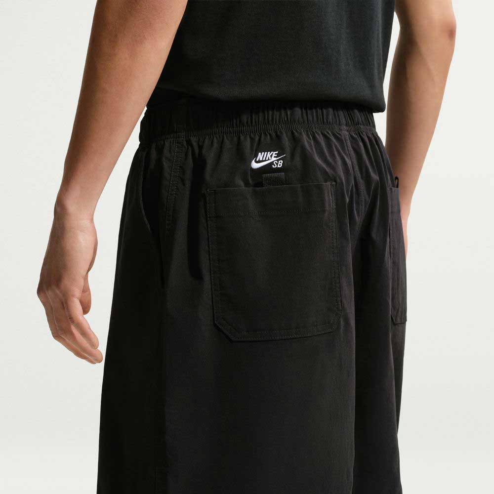 Person wearing IF1096010 Black White Skate Shorts Nike SB and a black shirt, shown from the back; sweat-wicking fabric and the Nike SB logo above the right rear pocket emphasize their skate-ready design.