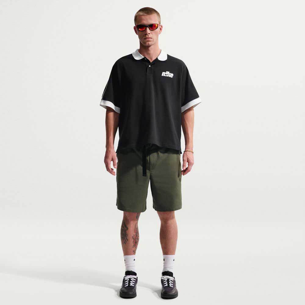A person wearing red sunglasses, a black short-sleeve polo, IF1096325 Cargo Khaki White Skate Shorts Nike SB, white socks, and black sneakers stands facing forward against a plain white background.