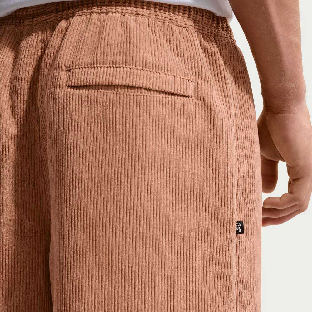 A close-up of a person wearing Nike SB II4426217 Light Cognac Black Corduroy Skate Shorts featuring a back pocket, elastic waistband, and a black side tag; their hand rests by their side.