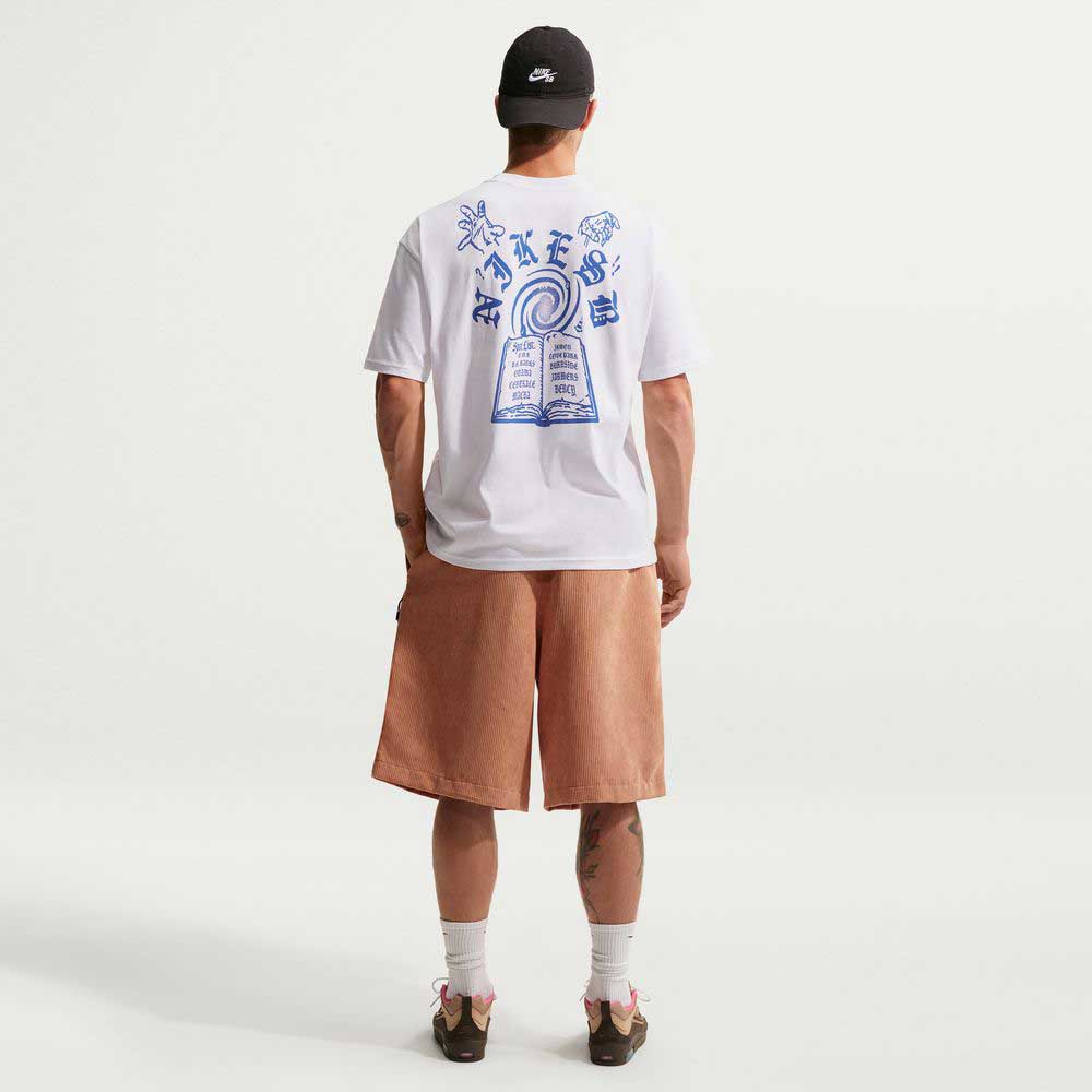 A man faces away, wearing a white T-shirt with blue graphics on the back, II4426217 Light Cognac Black Corduroy Skate Shorts Nike SB, white socks, brown shoes, and a black cap against a plain white background.