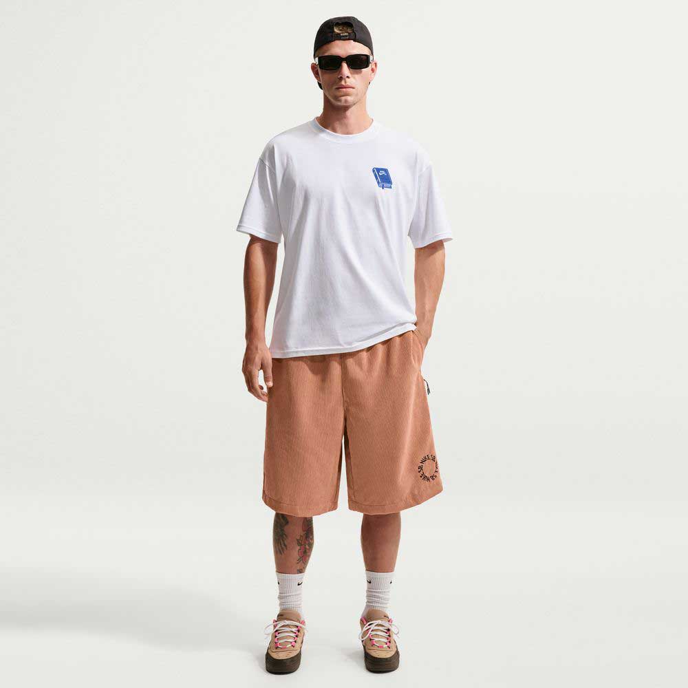 A man wearing sunglasses, a white T-shirt, II4426217 Light Cognac Black Corduroy Skate Shorts Nike SB, white socks, and sneakers stands against a plain white background with his hands in his pockets.