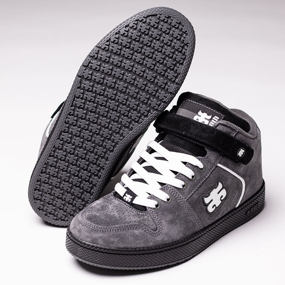 A pair of Grasshopper Gray Suede I Path Shoes for skateboarding, featuring black soles, white laces, and a side logo. One shoe stands upright while the other reveals its textured sole, evoking the classic Grasshopper silhouette.