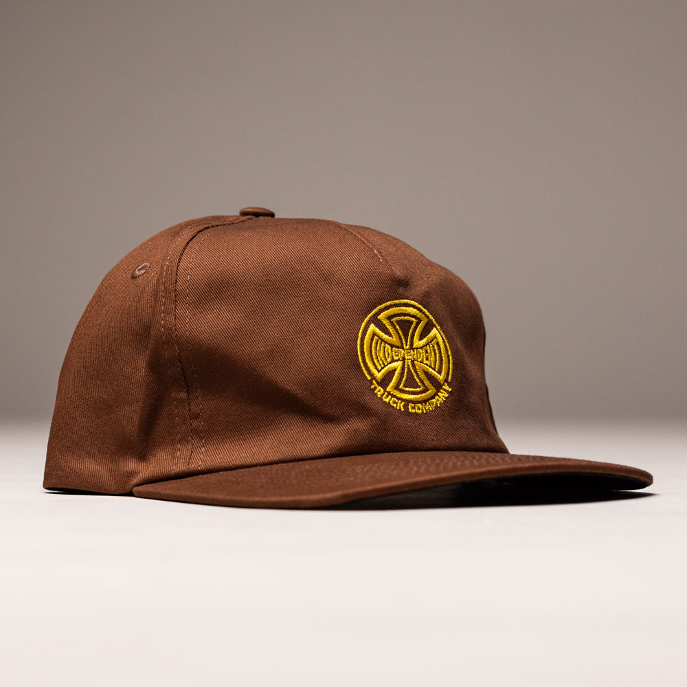 The Truck Co Legacy Brown Hat features a tan snapback and unstructured, low-profile fit with a yellow embroidered circular “Truck Company” logo on the front. Unisex, one size. Shown against a neutral background by Independent Skateboards.
