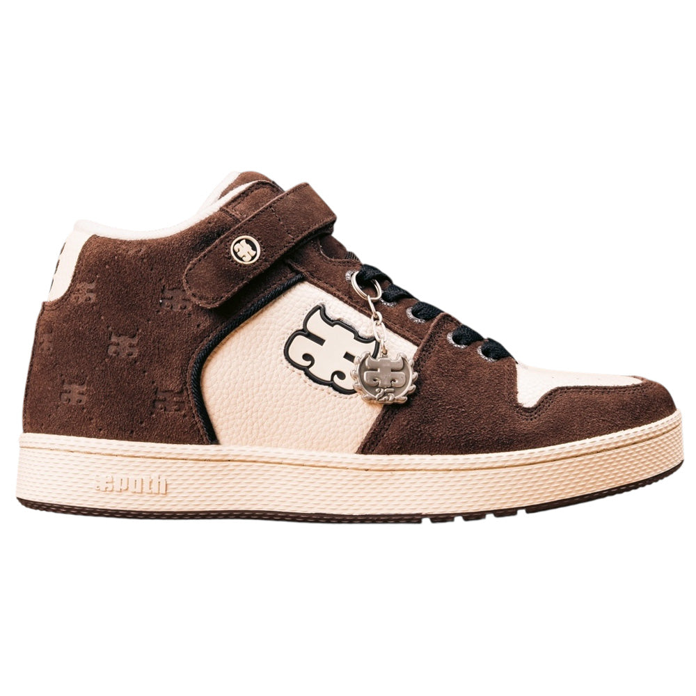 The Grasshopper Brown Suede Leather I Path Shoes feature suede panels, black laces, a Velcro strap, a metallic puzzle piece charm, an embossed logo, and a textured sole, taking inspiration from classic Grasshopper skateboarding shoes.