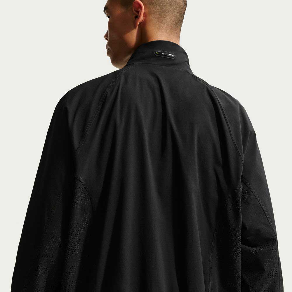 A person with short hair is seen from behind, wearing a black Ishod Cargo Track Jacket Black IF0438010 by Nike SB with a high collar, set against a plain light background.