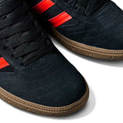 Close-up of JH8134 Black Orange Gum Busenitz Adidas Skateboarding suede shoes with gum soles, black laces, and three bright orange stripes on the side, photographed against a white background.