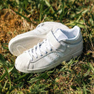 JH8141 White Silver White Pro Shell Mid Trainers ADV Adidas Suede Skateboarding Shoes are placed on dry grass and green leaves outdoors in sunlight, showcasing their vintage basketball-inspired style with laces and Velcro straps.