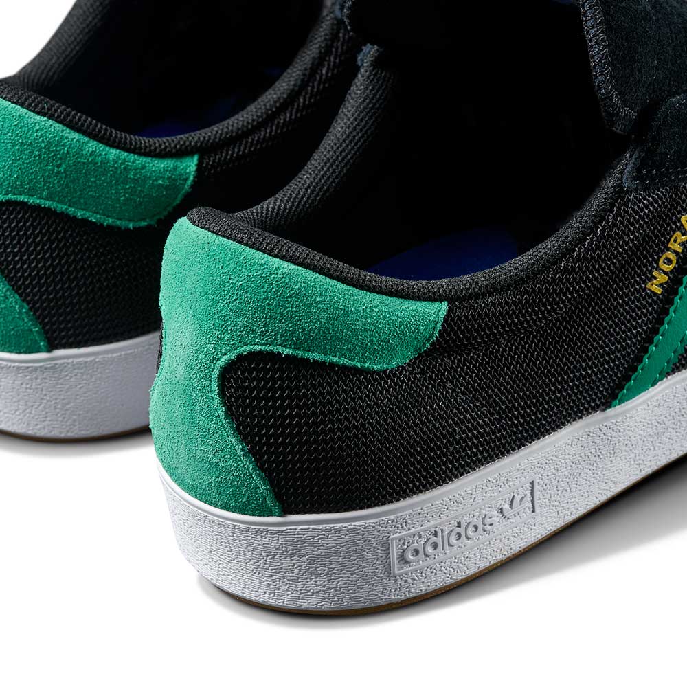 Close-up of the JH8143 Nora Black Green Suede Adidas Skateboarding Shoes, featuring black and green suede, white soles with an embossed Adidas logo, and a partially visible gold label for a classic, vintage-inspired style.