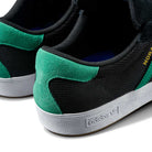 Close-up of the JH8143 Nora Black Green Suede Adidas Skateboarding Shoes, featuring black and green suede, white soles with an embossed Adidas logo, and a partially visible gold label for a classic, vintage-inspired style.
