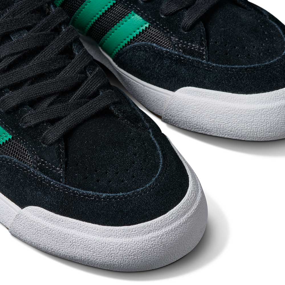 Close-up of JH8143 Nora Black Green Suede Adidas Skateboarding Shoes featuring green stripes, black laces, and white rubber soles, displayed on a white background.