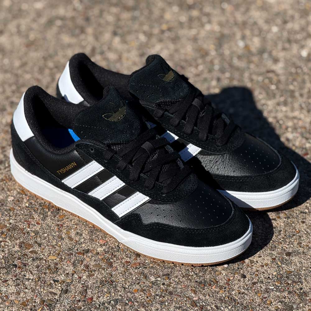 A pair of JI 0846 Black White Gum Tyshawn 2 II Adidas Skateboarding Leather Suede Shoes, with classic white stripes and soles, rests on a rough, sunlit surface.