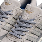 Close-up of a pair of Adidas JI0848 Granite White Tyshawn 2 II leather suede skateboarding shoes, featuring signature three stripes, gold trefoil logo on the padded tongue, and gray laces.