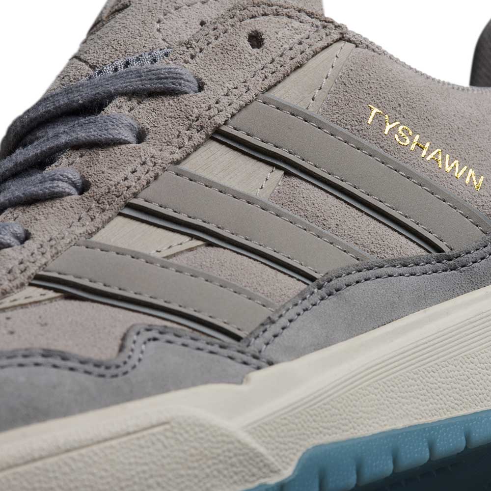 Close-up of the JI0848 Granite White Tyshawn 2 Adidas Skateboarding Shoe, featuring grey suede, three grey stripes, a blue-tinted outsole, and "TYSHAWN" gold lettering on the side.